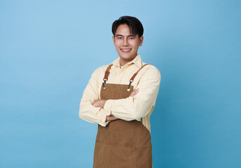 Portrait young asian barista man wearing apron standing and smile arms crossed isolated on blue...