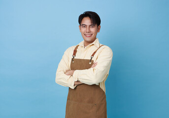 Portrait young asian barista man wearing apron standing and smile arms crossed isolated on blue background, waitress or entrepreneur cheerful, small business or startup,