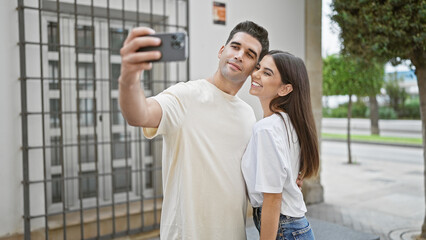 Couple takes a selfie on a sunny urban street, embodying love, relationship and togetherness amidst a city backdrop.