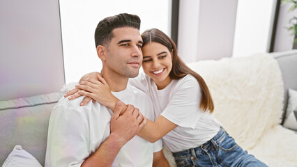 Affectionate woman hugging smiling man from behind on a cozy sofa in a modern living room