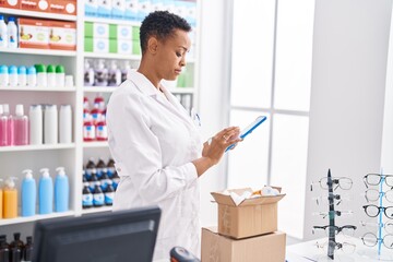 African american woman pharmacist using touchpad holding packages at pharmacy