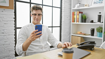 Hardworking young caucasian man in business, beaming while typing a message via smartphone at the...