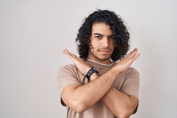 Hispanic man with curly hair standing over white background rejection expression crossing arms...