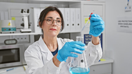 Mature woman scientist analyzing liquid in flask at indoor laboratory