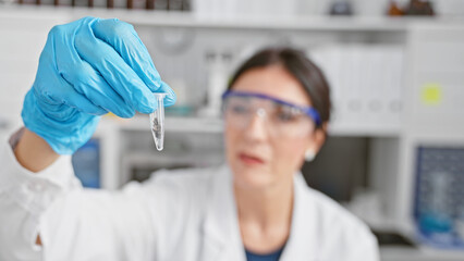 Hispanic woman examines a vial in laboratory indoor setting, portraying a professional healthcare environment.