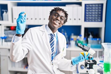 African american man scientist smiling confident holding pill and lemon at laboratory