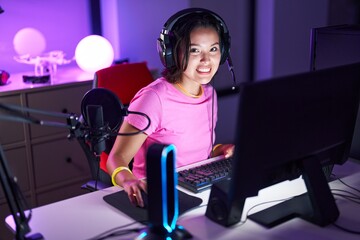 Young hispanic woman streamer playing video game using computer at gaming room