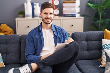 Obraz premium Young caucasian man writing on notebook sitting on sofa at home