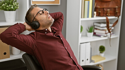 Relaxed businessman with headphones reclining in an office chair, eyes closed, enjoying a break.