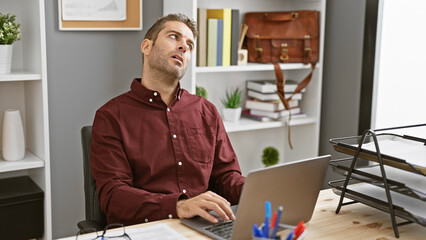 Pensive hispanic man with beard in office looking upwards, reflects professional contemplation or break at work.