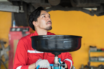 Male mechanic changing engine oil in auto repair shop. Male technician maintenance engine fluid in...
