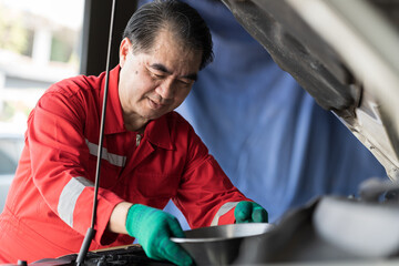 Senior male mechanic changing engine oil in auto repair shop. Male technician maintenance engine...