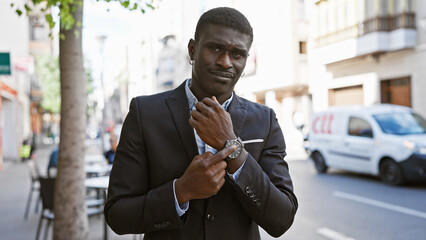 Handsome black man in suit adjusting watch on urban street