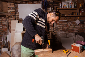 A carpenter works in a furniture workshop with various tools and a board
