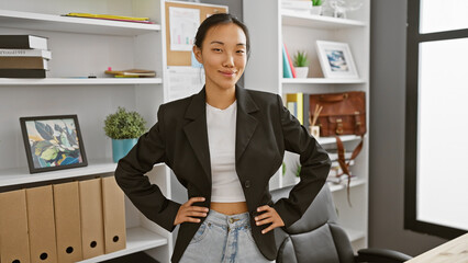 A confident young asian woman in a modern office setting, posing in business attire with shelving...