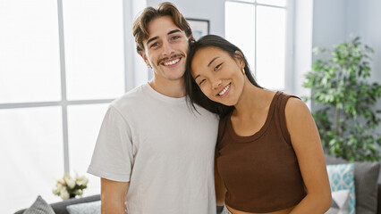 Joyful man and woman embrace in a bright apartment living room, showcasing their loving interracial...