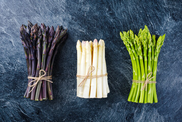 Fresh raw green, white and purple asparagus offered as a bundle as top view on gray background with...