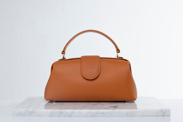 Luxury women's bag made of leather in brown and orange color tones, on a marble floor and white...