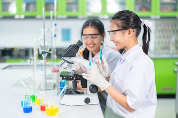 Side view of two Asian female scientists conducting research using a microscope. In the biology...