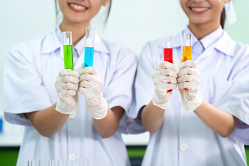 Close-up photo of chemical glass tubes in a laboratory. In the hands of two Asian female scientists, they research and produce medicines and vaccines for treating diseases using microscopy.