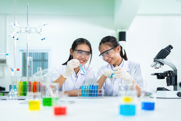 Two Asian female scientists, both doctors, hold chemical test tubes with medicine solutions. In the...