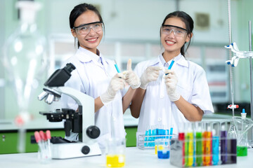 2 female scientist presenters are doctors Working in a chemistry lab Smiling and pointing at test tubes for producing vaccines, beakers, microscopes for making vaccines and treating diseases.