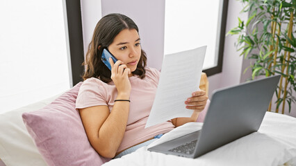 Hispanic young woman multitasking with phone and document in bedroom