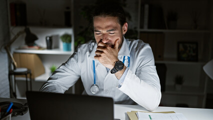 Young hispanic man doctor using laptop tired yawning at the clinic