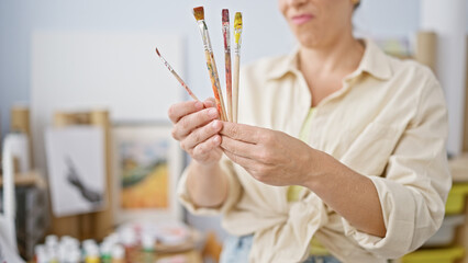 Young blonde woman artist looking paintbrushes thinking at art studio