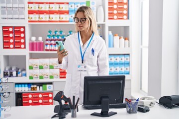 Young blonde woman pharmacist using smartphone and computer at pharmacy