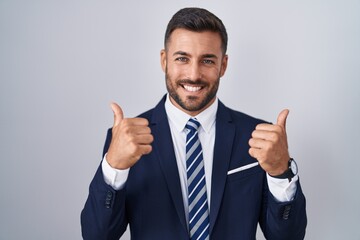 Handsome hispanic man wearing suit and tie success sign doing positive gesture with hand, thumbs up smiling and happy. cheerful expression and winner gesture.