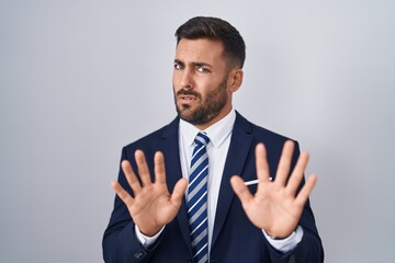 Handsome hispanic man wearing suit and tie moving away hands palms showing refusal and denial with...