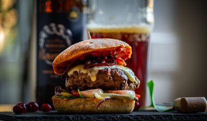 Homemade bacon cheeseburger on a dark tile with berries on the side and cold beer in the background. Food porn and nasty burger, smash burger - obrazy, fototapety, plakaty