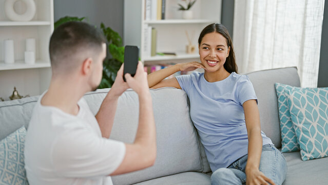 Beautiful couple, sitting together on their sofa at home, enjoy making a fun, casual mobile phone photo. love, smiles, and the indoor lifestyle captured in a beautiful relationship moment.