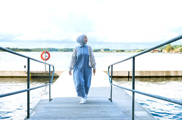 A confident Muslim woman walks by the lake on a pontoon. Norwegian nature near the city