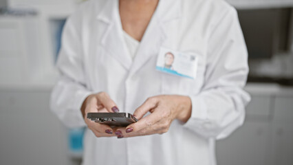Blurred professional woman with id badge in a laboratory holding a smartphone, depicting healthcare...