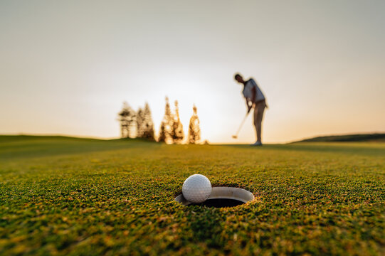 green, golf, ball, club, course, golfer, grass, sport, golfing, fairway. golf ball putting golf player, golf ball spinning to the hole on the green of the golf course with the early light of sunset.