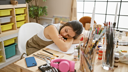 Exhausted yet focused, young, beautiful hispanic woman artist drawing in notebook, leaning over...