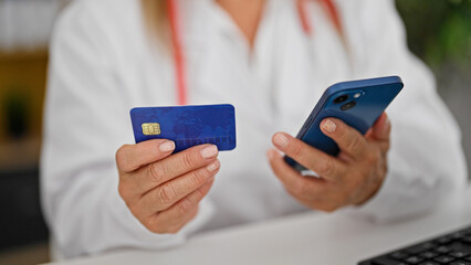 Fototapeta premium Middle age hispanic woman doctor shopping with smartphone and credit card at the clinic