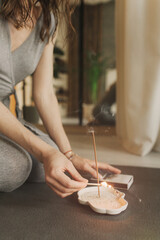A young woman lighting incense sticks an home before yoga. Buddhist healing practices. Clearing the...