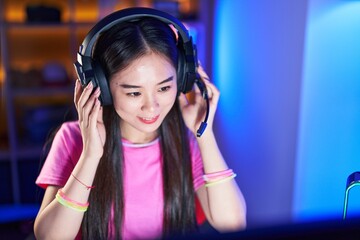 Young chinese woman streamer smiling confident sitting on bed at gaming room