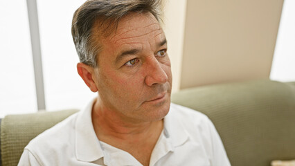 Handsome middle-aged man in white shirt contemplating indoors with a couch background