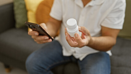 Obraz na płótnie Canvas Mature man holding medication and smartphone in a modern living room, contemplating prescription refill