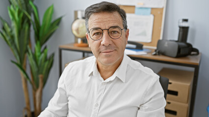 A mature man in glasses poses confidently in a modern office, symbolizing professionalism and...