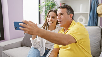 Fototapeta premium Heartwarming scene of a father and daughter joyfully sitting on the sofa at home, deep in conversation during a cozy indoor video call, showcasing their love and positive family relationship.