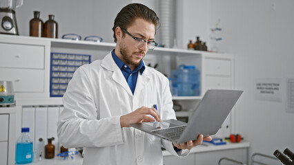 Young hispanic man scientist using laptop at laboratory