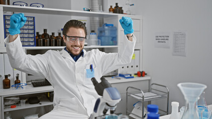 Fototapeta na wymiar Young hispanic man scientist smiling confident using microscope celebrating at laboratory