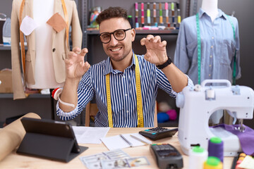 Hispanic man with beard dressmaker designer working at atelier smiling funny doing claw gesture as...