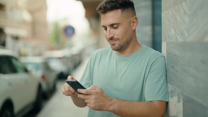 Young hispanic man smiling confident using smartphone at street