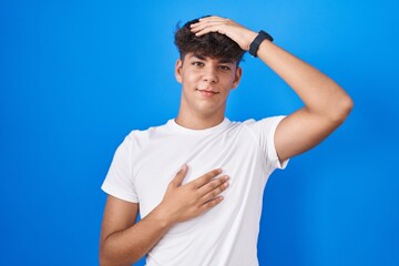 Naklejka premium Hispanic teenager standing over blue background touching forehead for illness and fever, flu and cold, virus sick